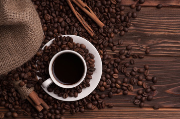 top view coffee cup with coffee beans on textile and cinnamon on dark wood background table