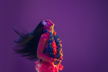 Motion, flying hairs. Hawaiian brunette model on purple studio background in neon light. Beautiful...