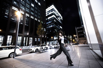 Stylish african american woman walking in night city. Houses illuminated, machines and bicycles on the background. Nightlife in Frankfurt. Evening city walks. Lifestyle concepts