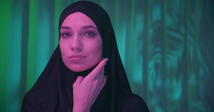 Beautiful confident girl in black hijab neon night green tropical background shadow image make-up purple color profile view turn