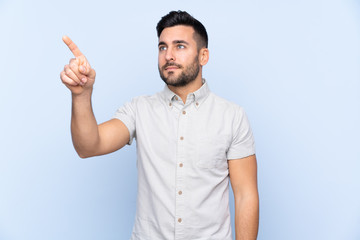 Young handsome man with beard over isolated blue background touching on transparent screen
