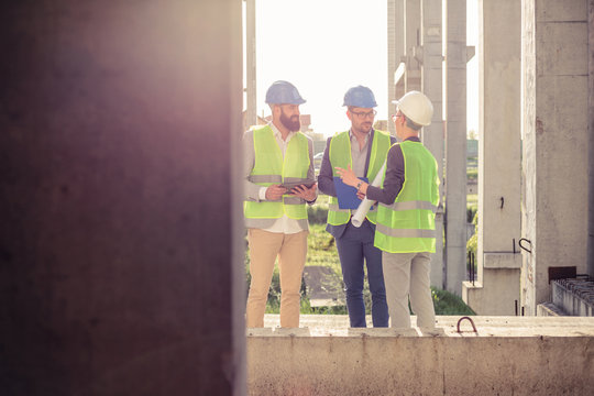 Small mixed group of young architects, wearing suits and safety equipment, meeting and discussing on a construction site