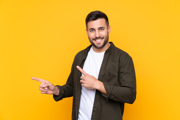 Man over isolated yellow background pointing finger to the side