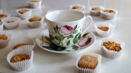 porcelain cup with a pattern in the form of a rose and cookies on a white table