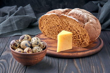 Pumpernickel - bread made with a combination of rye flour and whole rye grains. Quail eggs in a clay bowl, cheese. Fresh healthy farm food.