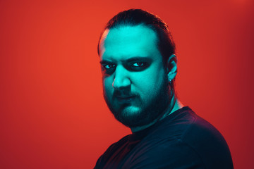 Portrait of a guy with colorful neon light on red studio background. Male model with calm and serious mood. Facial expression, cyberpunk, millenials lifestyle and look like. Future, technologies.
