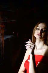 A beautiful young girl in a red dress and a red hat on a white background in the studio. Luxury jewelry, necklaces and rings, bright makeup, red lips, manicure. Glamorous luxury lady