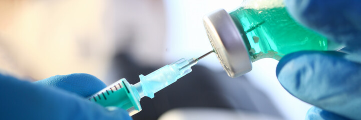 Scientist hand in blue protective gloves filling syringe with some experimental liquid