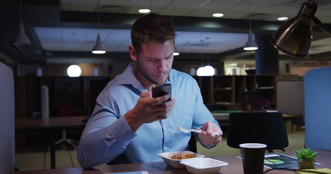 Businessman working and eating in a modern office by night