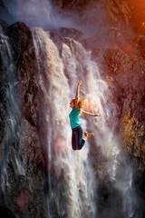 Eine Frau springt vor Freude vor einem Wasserfall