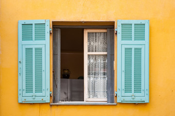Open light blue window shutters on pale orange wall in rural south of France