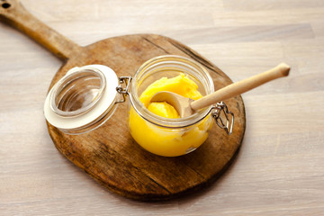 Ghee clarified butter desi in glass jar with spoon made from wood on natural wooden background