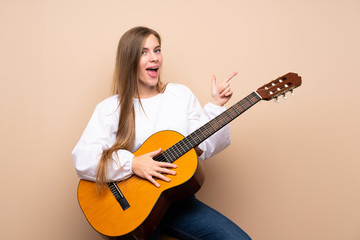 Teenager girl with guitar over isolated background surprised and pointing finger to the side