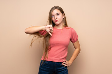 Teenager blonde girl over isolated background showing thumb down sign