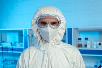 Fototapeta na wymiar scientist in hazmat suit, medical mask and goggles looking at camera