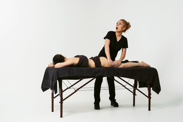 Funny fat burning massage. Portrait of cheerful woman masseur in uniforme near massage table with woman patient in wellness center. White background isolated