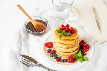 Stack of pancakes with fresh red currant, blueberries, raspberries and honey on a light background for the tasty breakfast.