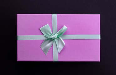 Top view purple present box with green bow on black background.