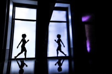 Side view full-length female silhouette on white window background. A woman running. Her figure is reflected on the wall and floor. Lifestyle