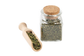 dried nettle herb or in latin Utricae folium in a glass jar and wooden scoop isolated on white background. medicinal healing herbs. herbal medicine. alternative medicine
