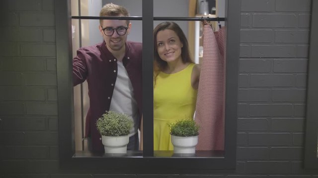 Young Couple In Love Opening Curtains And Looking Out The Window