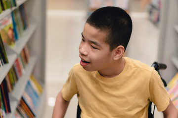 Disabled child on wheelchair having fun choosing books from shelves, Special children's lifestyle, Life in the education age of special need kids, Happy disability kid concept, Selective focus.