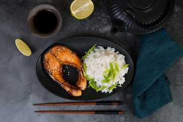Classic Asian dinner dish, baked fish and white rice on a dark background.