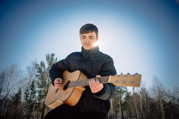 handsome guy playing guitar outside in sunny winter day