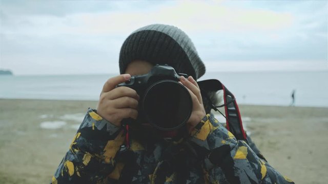 A child with a camera in his hands learns to take pictures against the sea in autumn