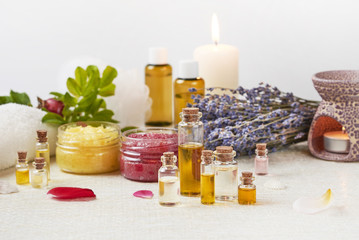 Aromatherapy products. A set of essential oils, scrub jars, lavender, dogrose, a white towel, an aromatherapy lamp, rose petals, a burning candle stand on a light table