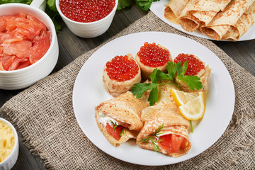Beautifully rolled pancakes(blini) with fresh sour cream, red caviar and red fish on a white plate....