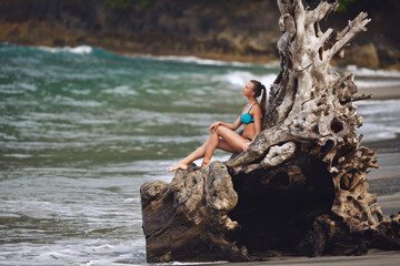 girl in a blue swimsuit stands at the root of a palm tree on a tropical beach