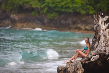 girl in a blue swimsuit stands at the root of a palm tree on a tropical beach