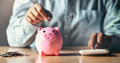 Obraz na płótnie Canvas businessman saving money concept. hand putting coins in piggybank and using calculator