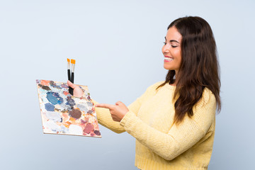 Young artist woman over isolated blue background pointing to the side to present a product