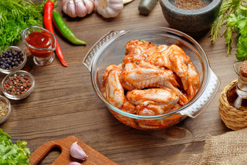Marinated chicken wings in a glass bowl. Glass dish with marinated wings on a wooden table