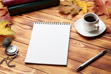Notebook with pen, old clock, cup of coffee, books and maple leaves, lie on a wooden table. Autumn composition. copy space
