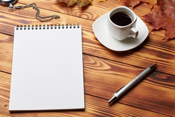 Notebook with pen, old clock, cup of coffee, books and maple leaves, lie on a wooden table. Copy space