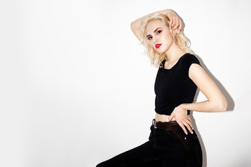 Fototapeta premium young sexy blonde girl in a black t-shirt and black jeans on a white background, studio fashion photo with copy space