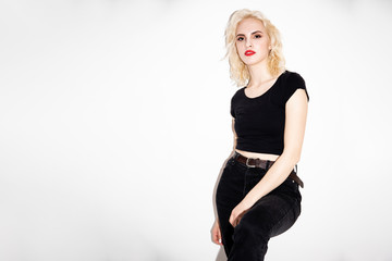 young blonde girl in a black t-shirt and black jeans on a white background, studio fashion photo with copy space