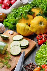 Sliced zucchini lying on a board surrounded by lettuce, patissons, cherry tomatoes, garlic and parsley