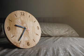 Wooden clock on the bed with morning light flare.
