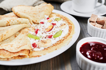 Thin pancakes (blini) with cream and grated chocolate with fruit slices on a white plate. Close-up. Strawberry Jam, Cane Sugar. Sweet dessert.