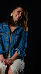 Young beautiful woman wearing in a black leather jacket, black top, short skirt and boots posing over black background. Studio shot of blonde woman against black background