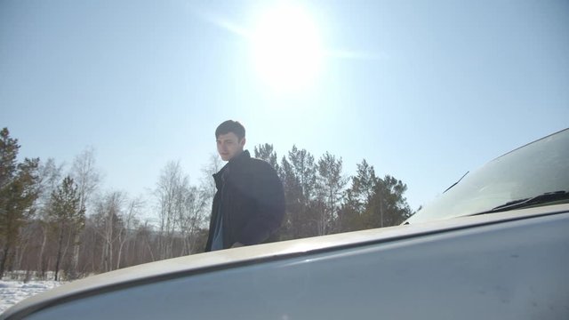 handsome guy fixing a car under a hood in sunny winter day in siberia