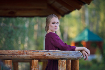 A girl in a burgundy dress walks on a suspended wooden bridge