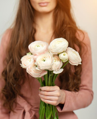 A girl in a pink dress is holding a bouquet of delicate Ranunculus flowers.