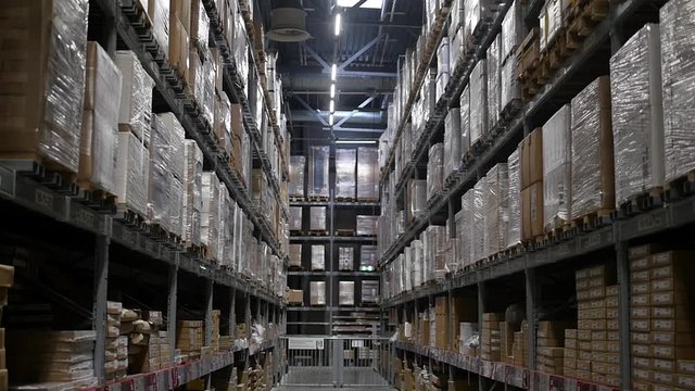 Products at the warehouse. Horizontal camera move between the rows shelves with cardboard boxes. Industrial interior storage room. Logistics center interior full of racks with with large number packs.
