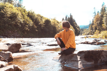 tourist girl sitting on the bank of a mountain river