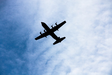 silhouette four engine propeller airplane on sky, photo shooting from under while airplane flying over with blue sky and white cloud as background. Photo with some noise